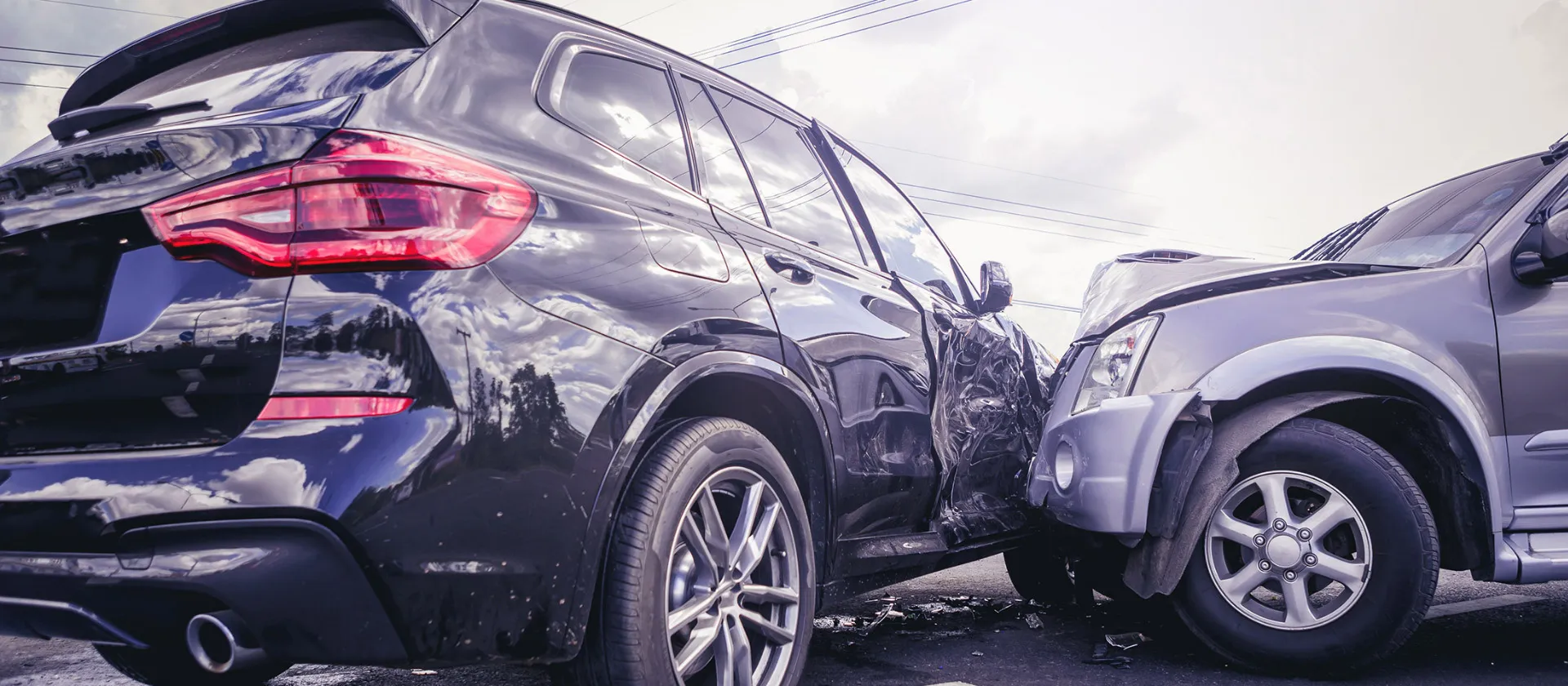 Two cars involved in a collision on the road, showing visible front and side damage under a cloudy sky.