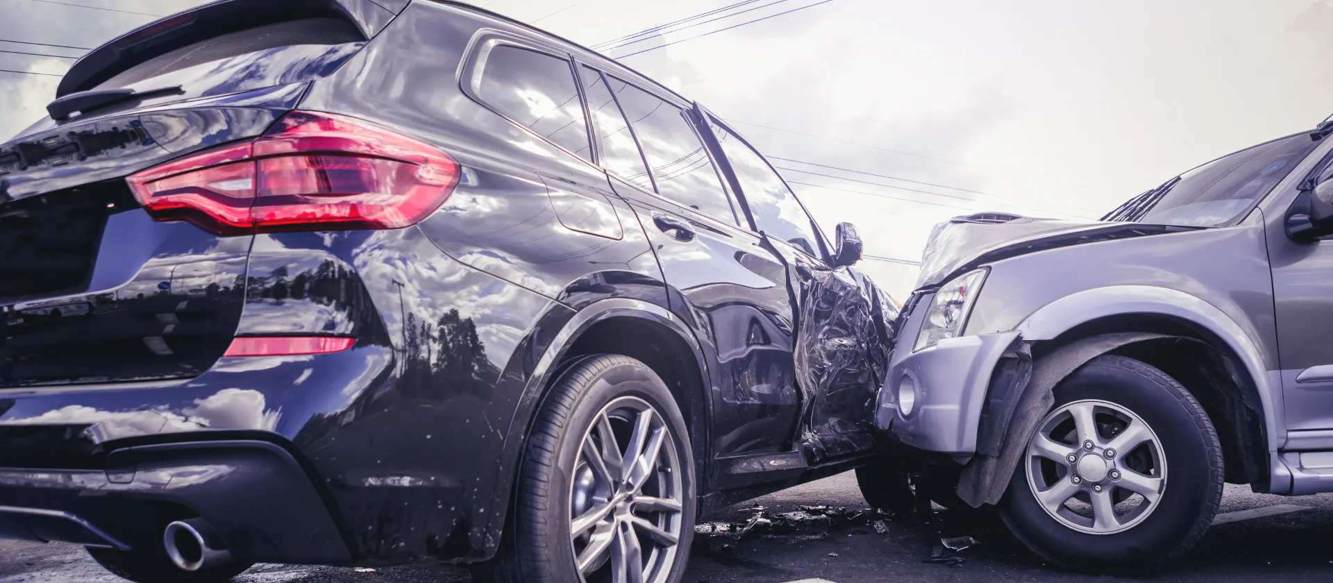 Two cars involved in a collision on the road, showing visible front and side damage under a cloudy sky.