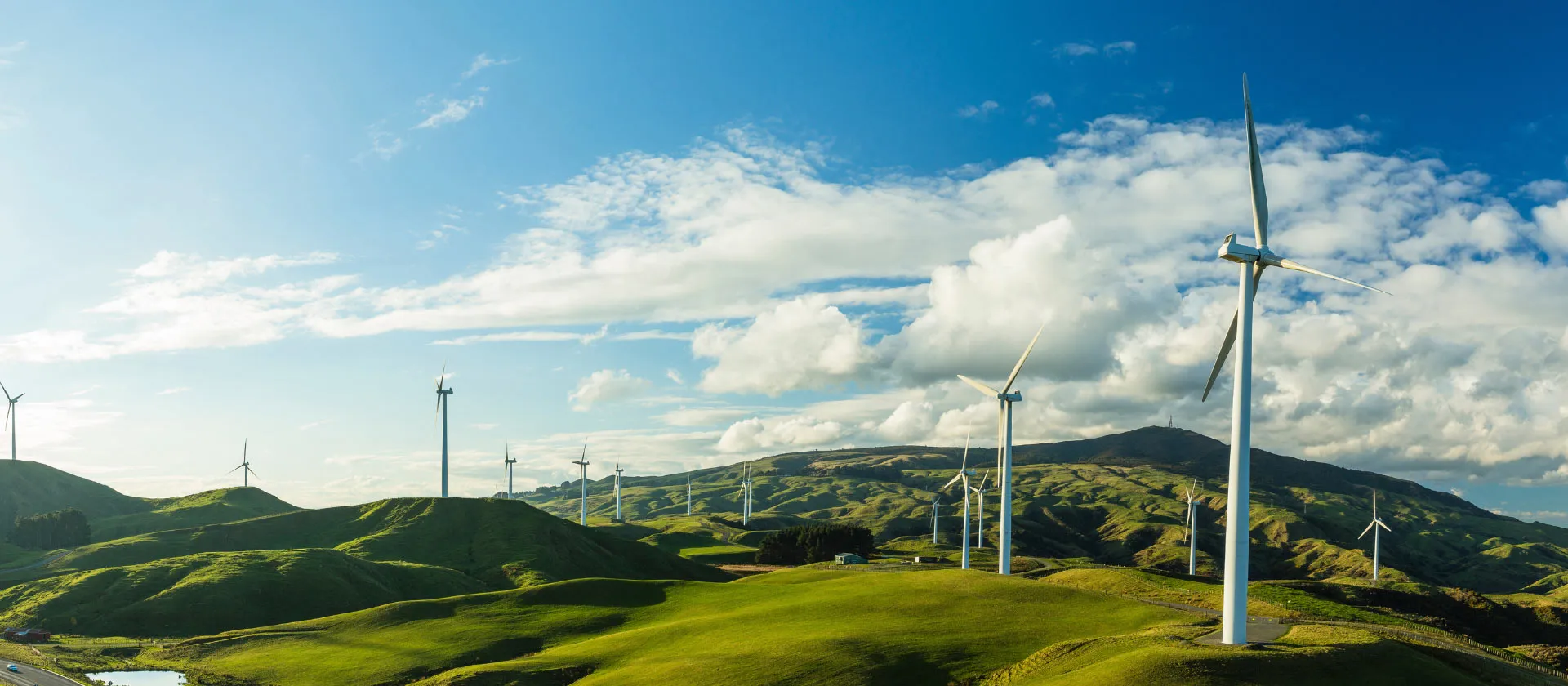 Wind turbines on rolling green hills under a bright sky, generating clean renewable energy