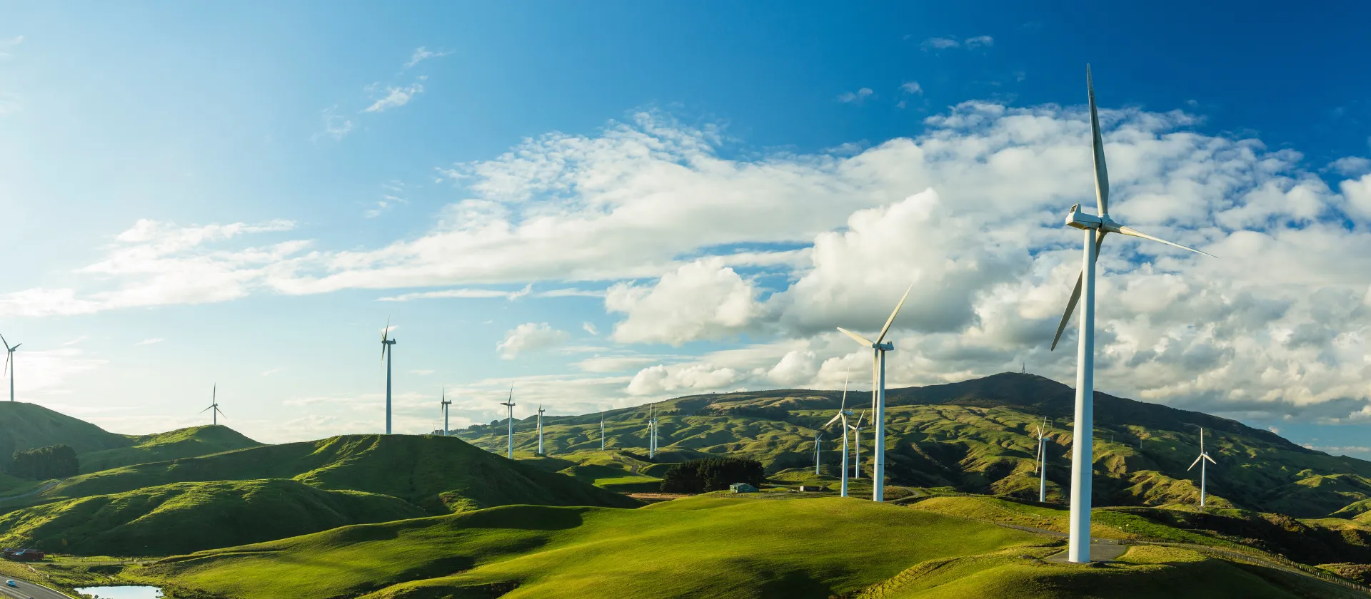 Wind turbines on rolling green hills under a bright sky, generating clean renewable energy