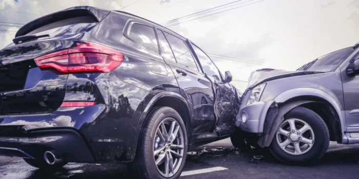 Two cars involved in a collision on the road, showing visible front and side damage under a cloudy sky.