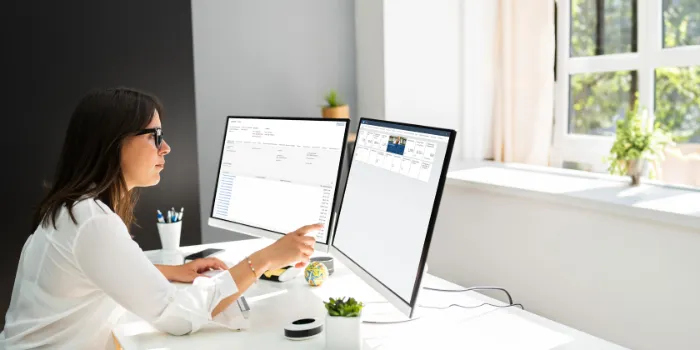 Professional working at desk on dual monitors displaying SAP FS-CD Collections and Disbursements dashboard and reporting tools