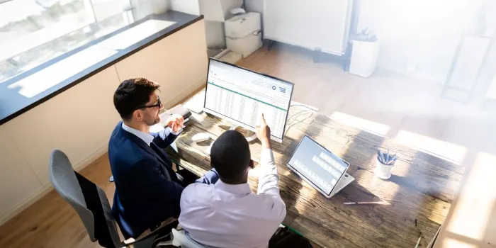 Two business professionals analyzing data on computer and tablet in office, discussing reports and strategy